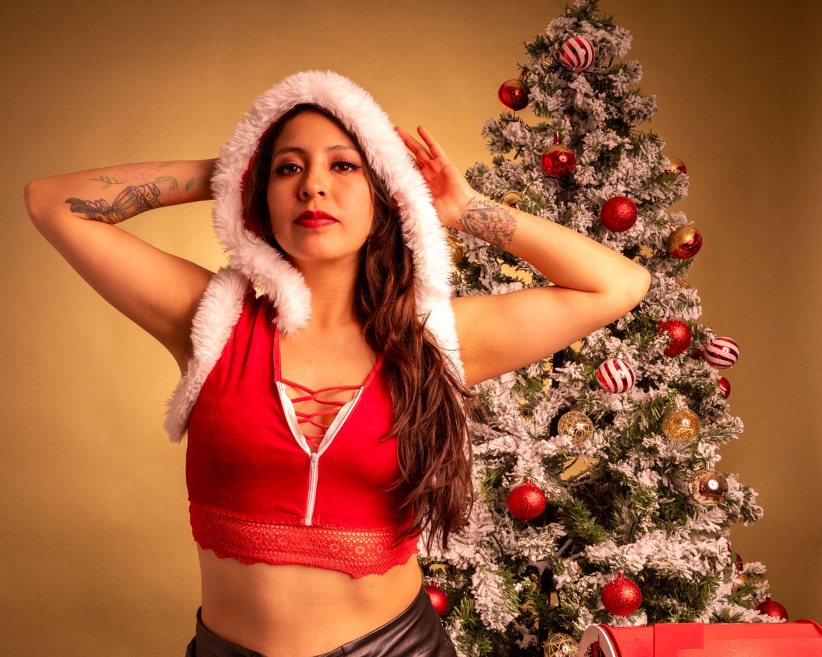 A woman in a red festive outfit poses confidently beside a decorated Christmas tree.
