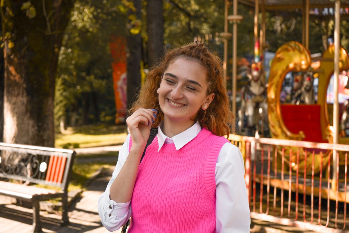 Smiling woman enjoys a sunny day at a park carousel wearing a vibrant pink vest.