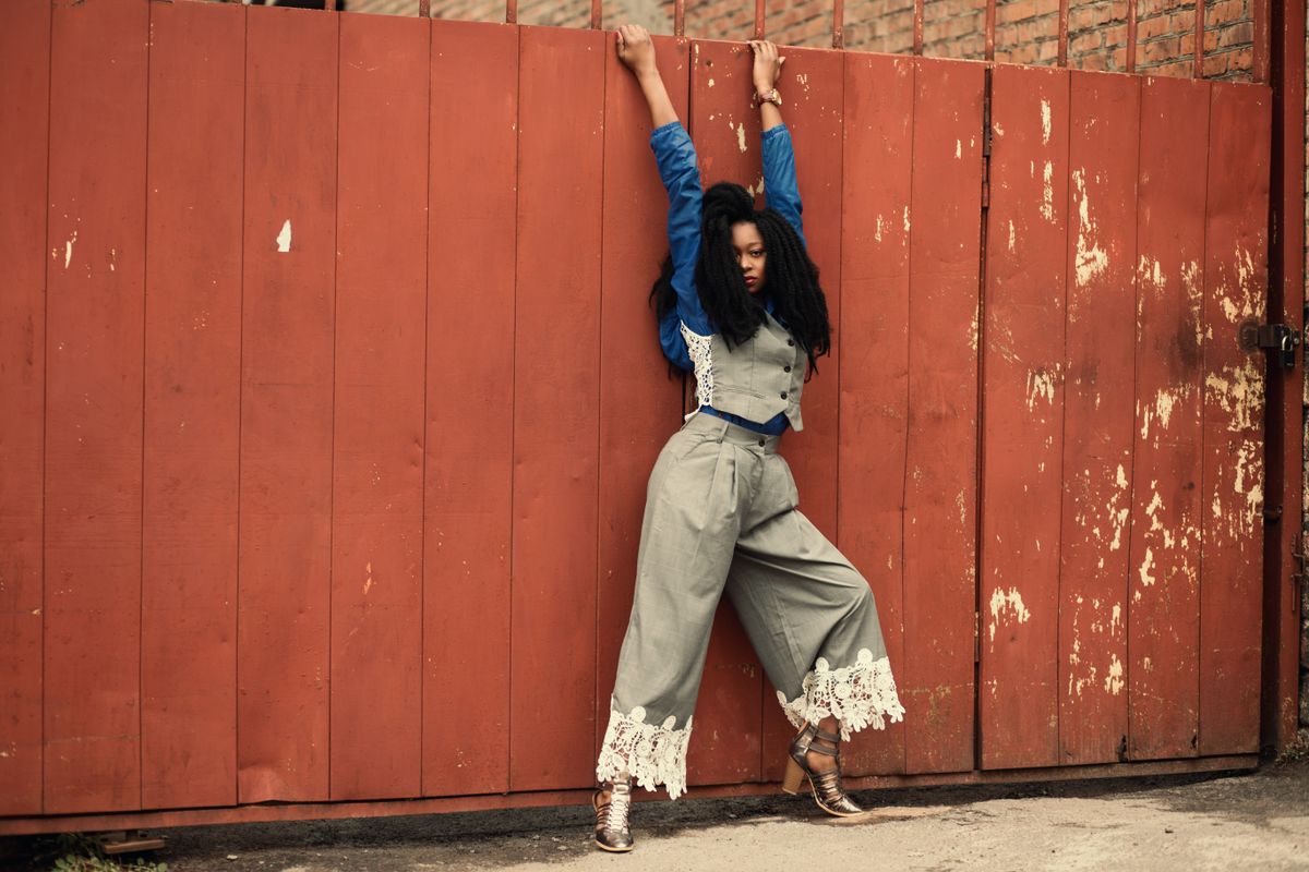 Fashionable woman wearing trendy lace outfit poses against a rustic red wall outdoors.