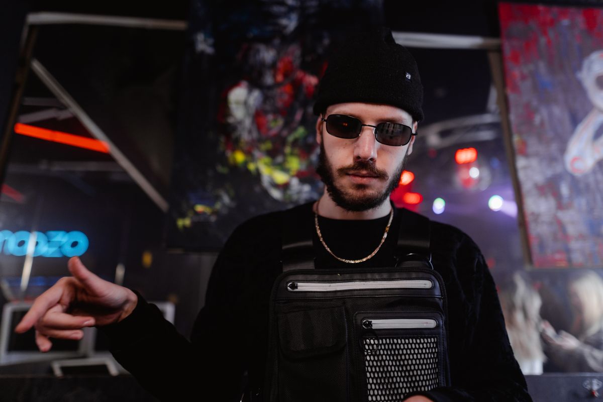 Stylish man in a dark outfit poses confidently in an urban setting, exuding a modern, edgy vibe.