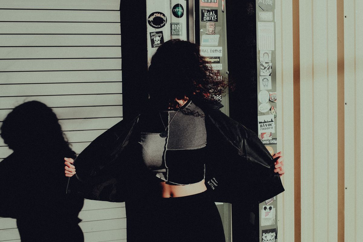 Artistic silhouette of a woman with curly hair in a black jacket, illuminated by dramatic shadows.