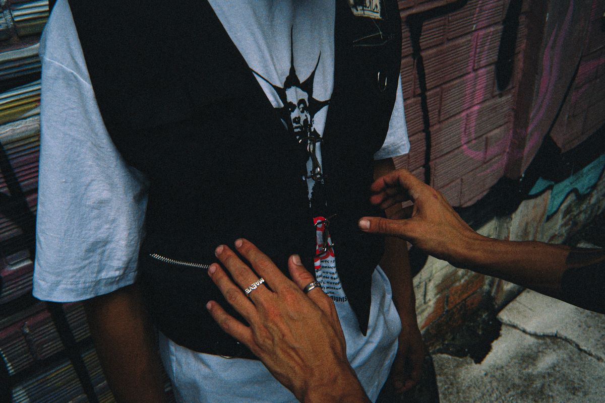 Close-up of street fashion with punk rock style vest and rings against urban graffiti background.