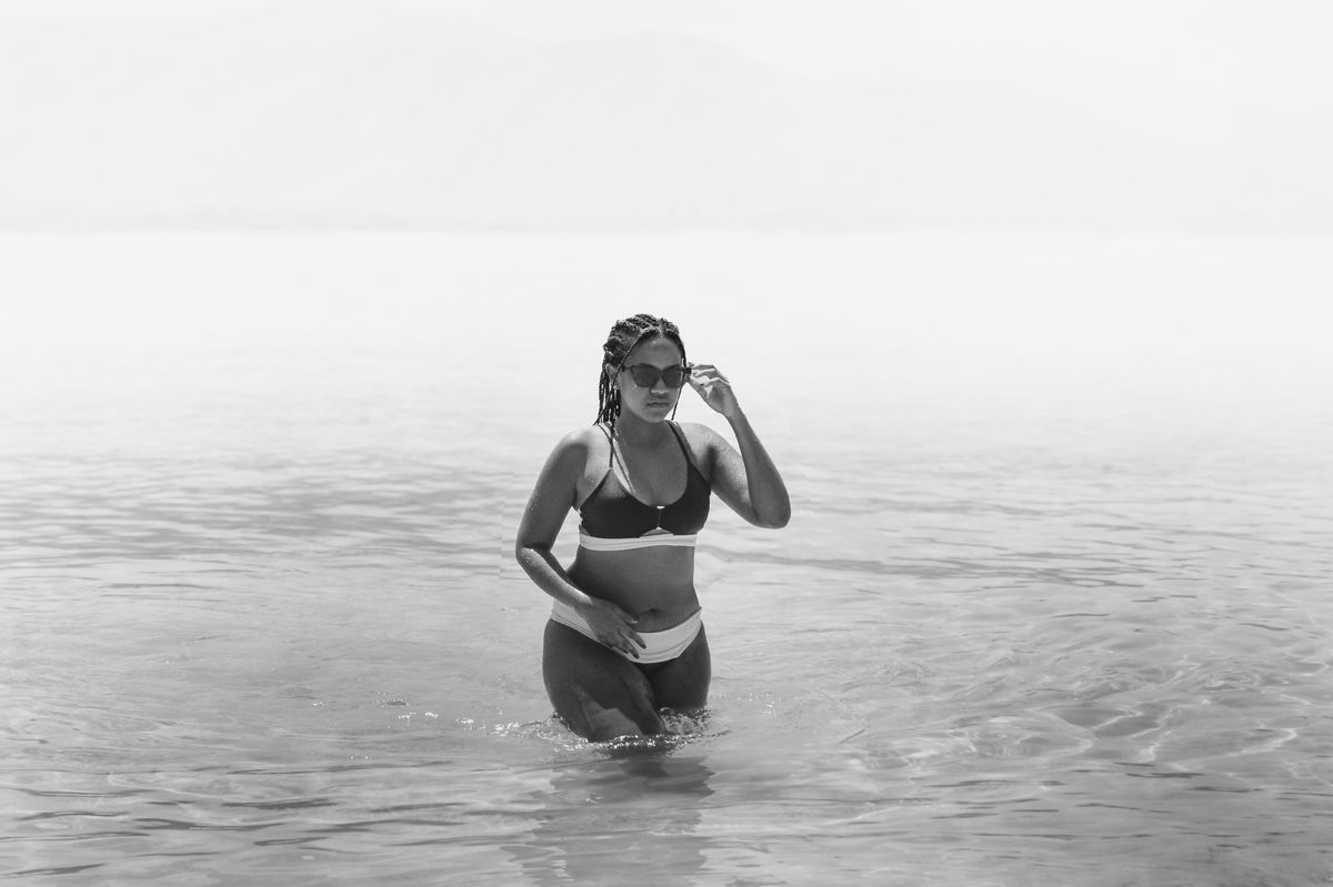 A woman walking through shallow ocean water in a black and white photograph.