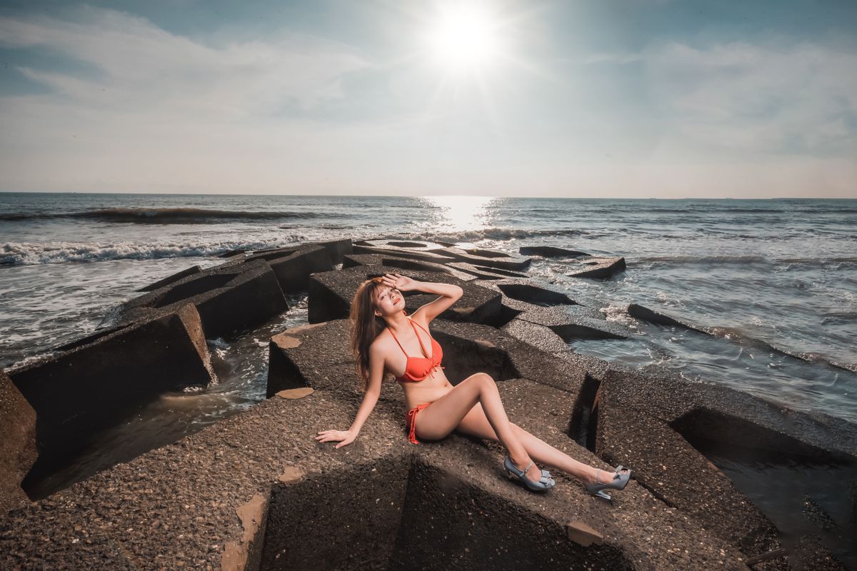 Woman in a red bikini relaxing on concrete blocks by the sea under bright sunlight.