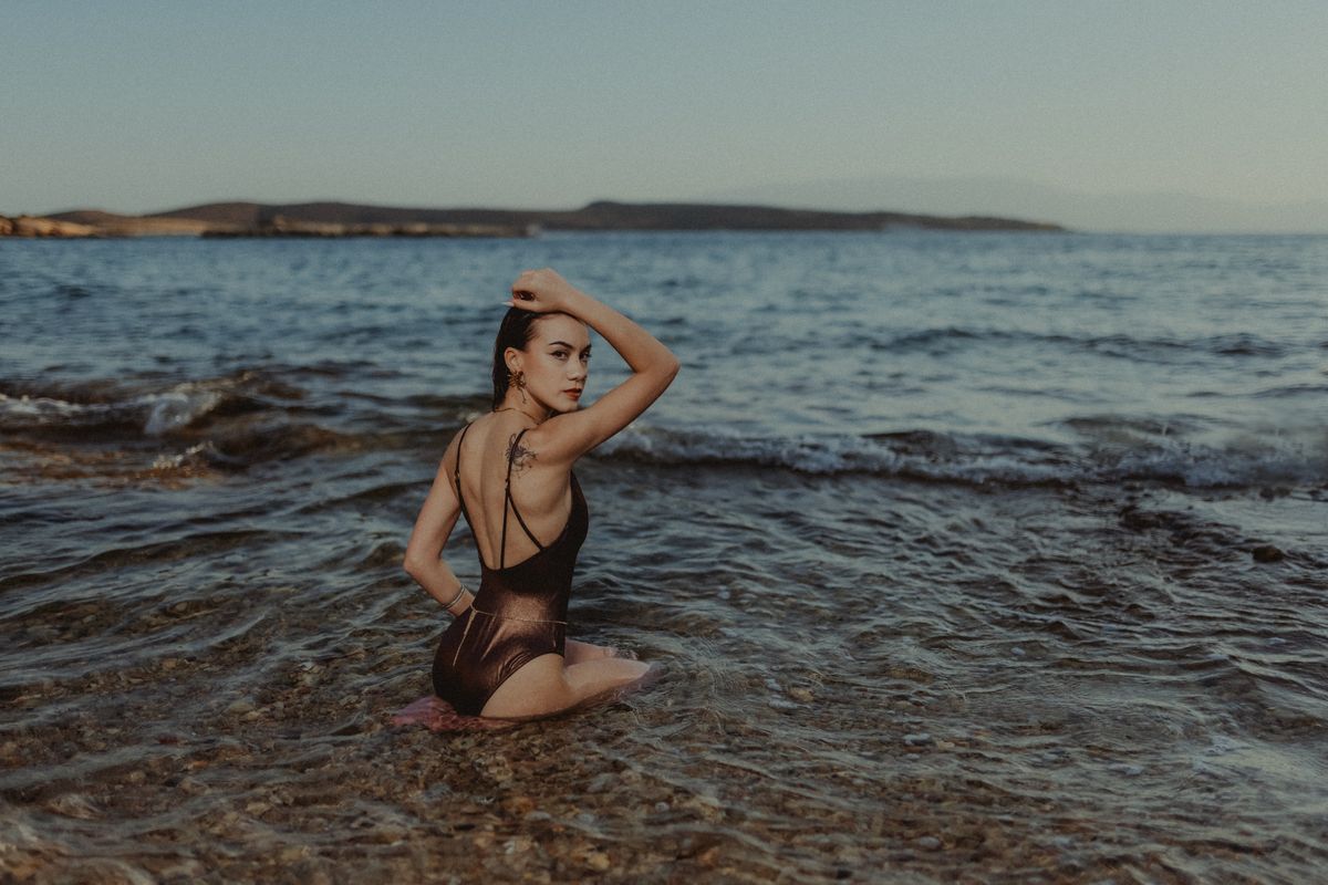 A woman in a swimsuit posing on a rocky beach by the ocean during the day.
