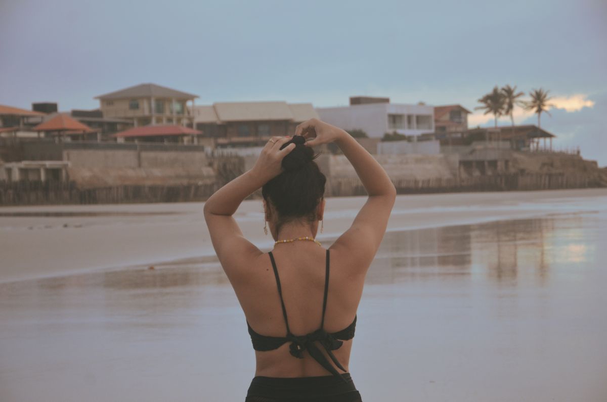 Woman in swimwear enjoys a tranquil beach view while fixing her hair in Salinópolis.
