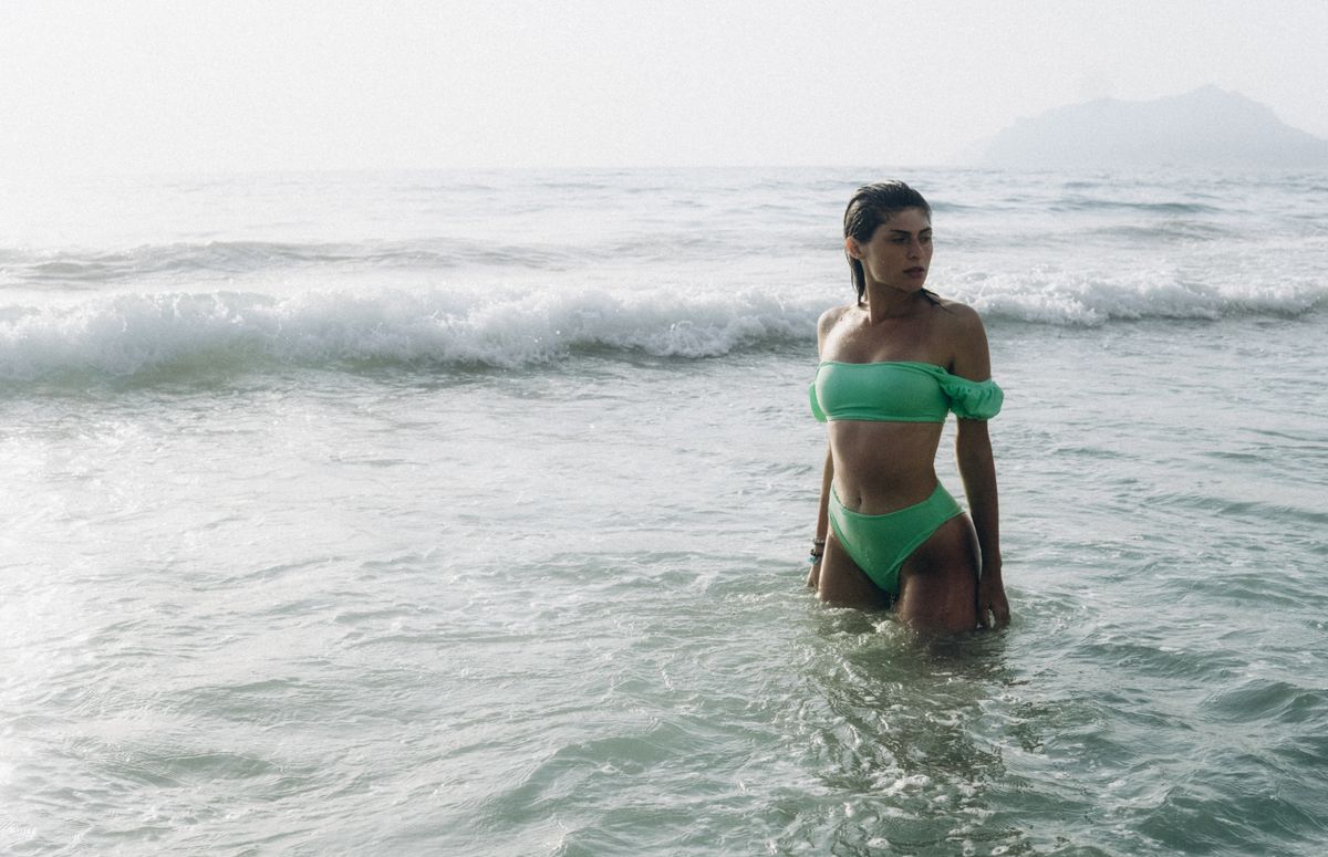 Woman in green bikini standing in the ocean waves on a sunny day.