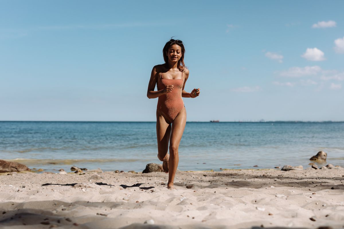 Young woman running on a sunny beach wearing a swimsuit, enjoying summer outdoors.
