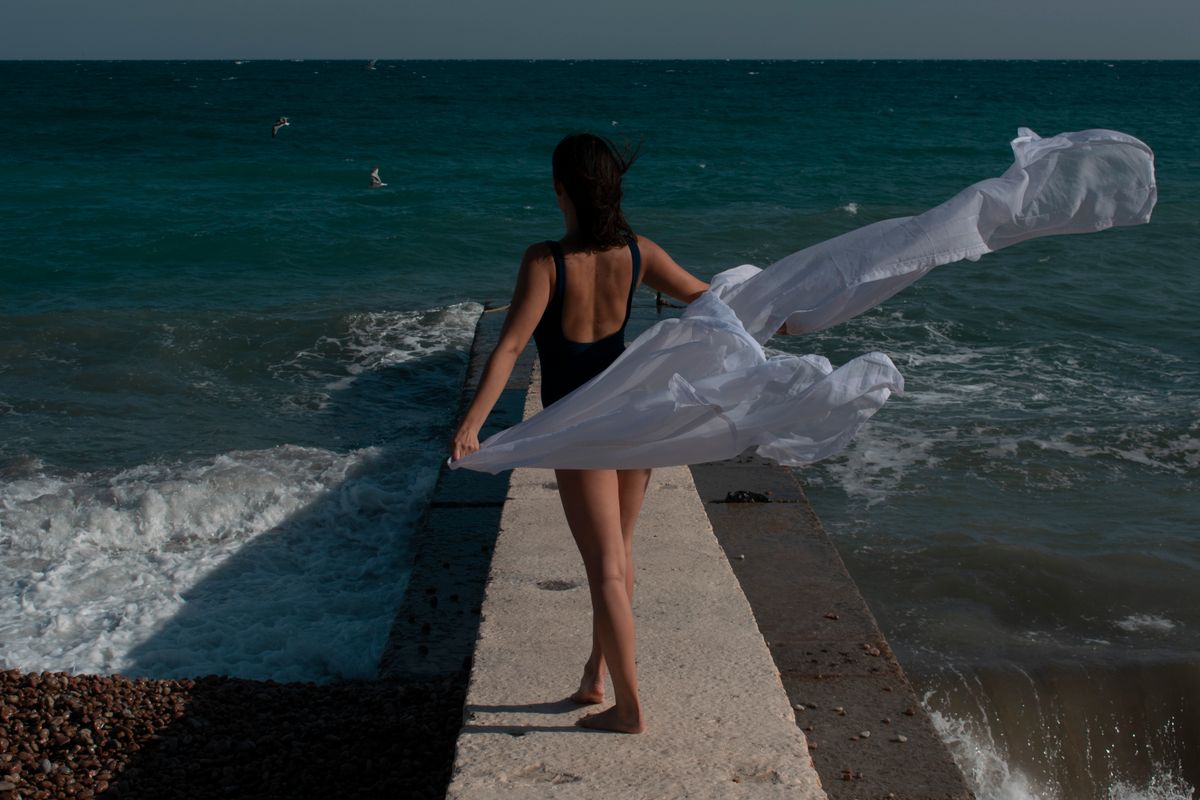 Woman standing on a dock at the beach holding white fabric, enjoying the ocean breeze.