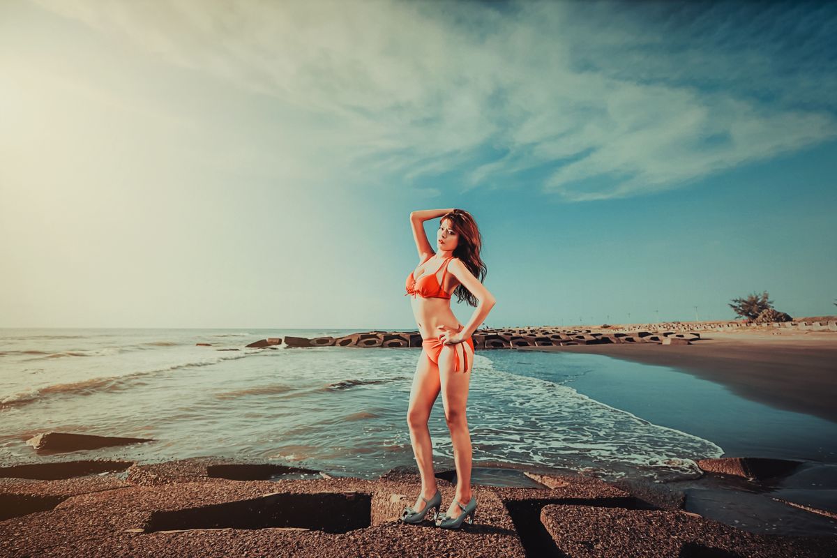 A woman posing elegantly in a bikini on a sunny beach with clear skies.