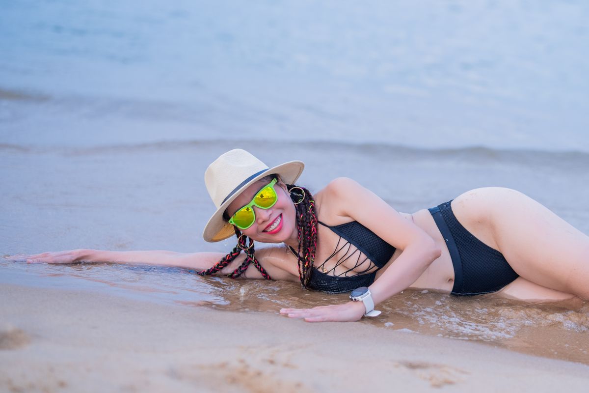 A woman in a bikini, sunglasses, and hat enjoying a day at the beach.