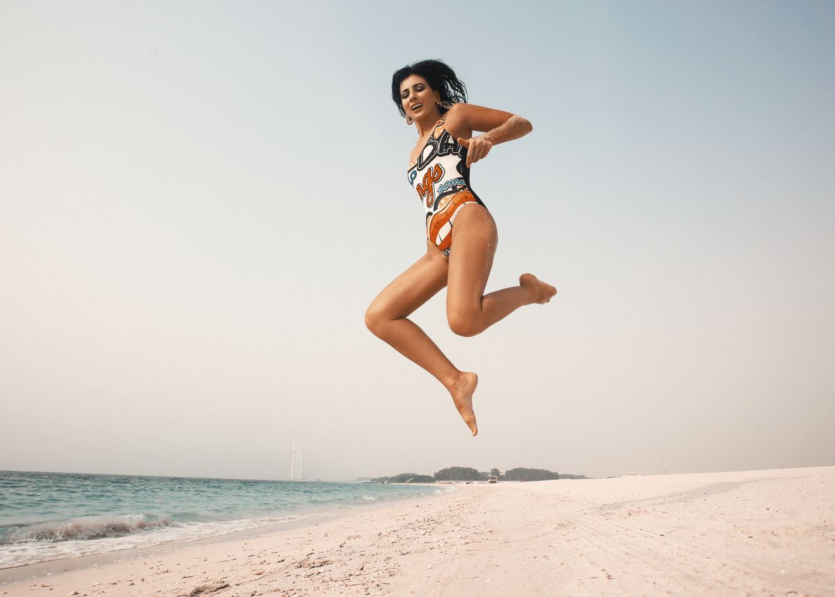 Energetic woman in swimsuit jumps on sunny beach, embracing summer joy and freedom.
