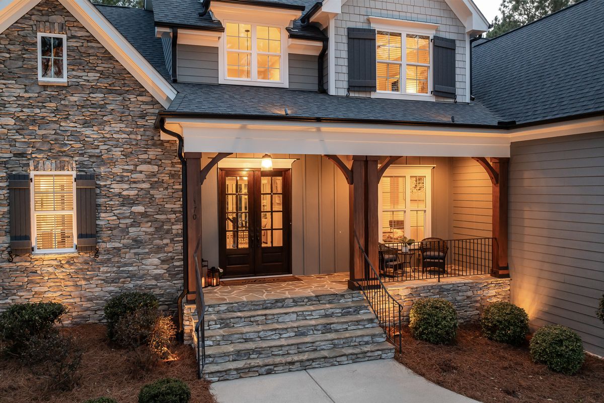 Inviting front porch of a cozy house with stone facade and warm lighting at dusk.