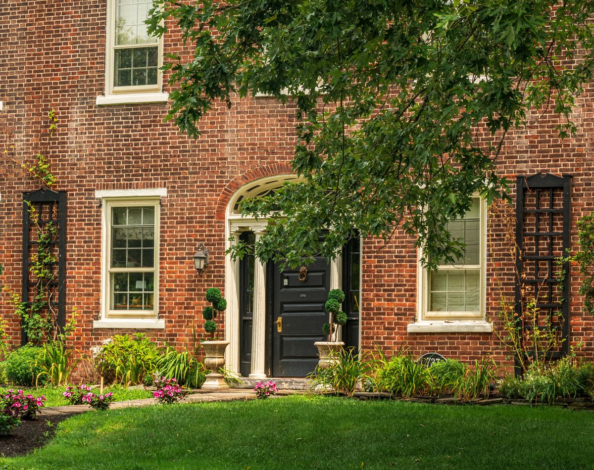 Charming red brick house with a classic black door, elegant garden, and lush greenery, capturing a serene architectural feel.