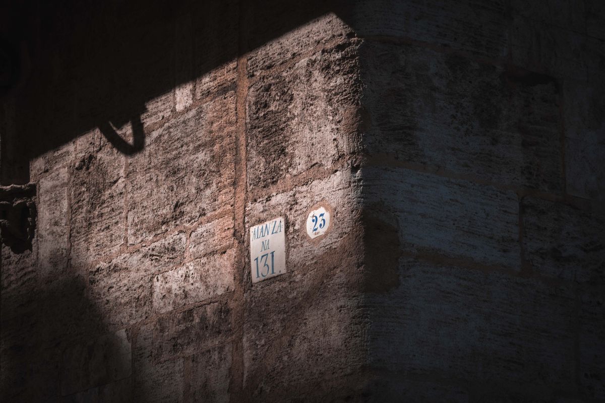 Close-up of an ancient wall corner with street numbers in dramatic lighting.
