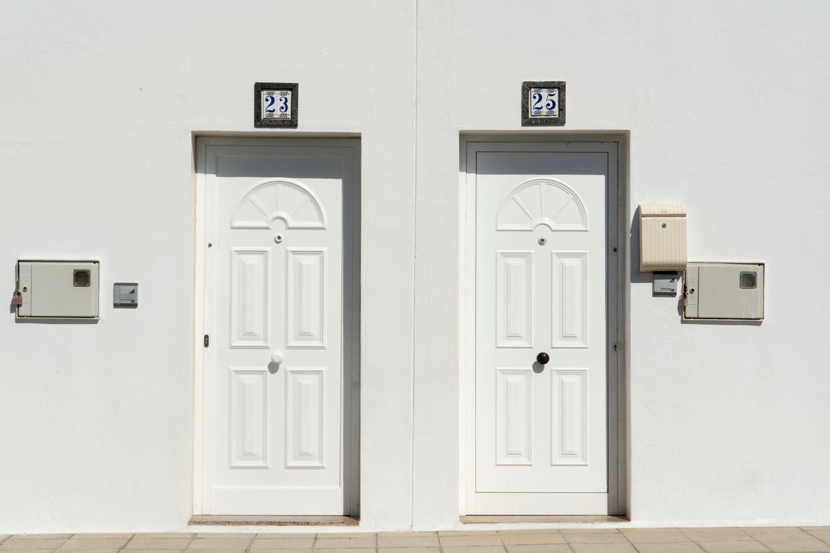 A minimalistic outdoor view of two white doors marked with numbers 23 and 25 on a white facade.