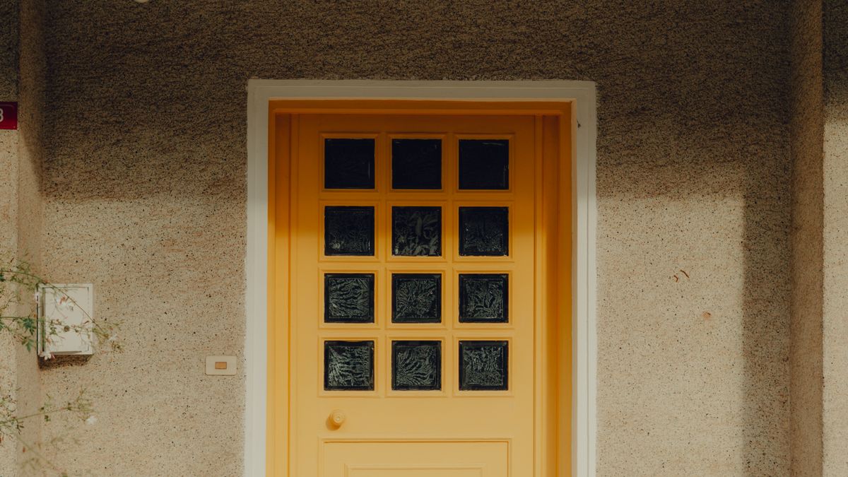A modern house entrance featuring a bright yellow door with glass panels, casting afternoon shadows.