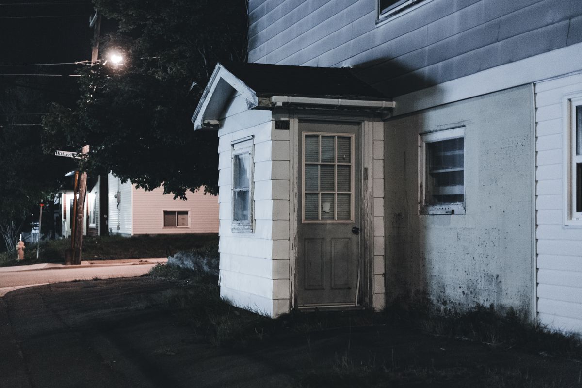 A moody nighttime view of a house entrance featuring a wooden porch and vintage architecture.