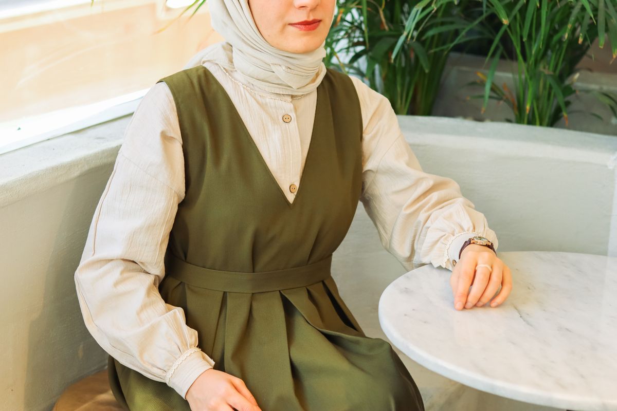 Woman in a green dress sitting at a café table with indoor plants.