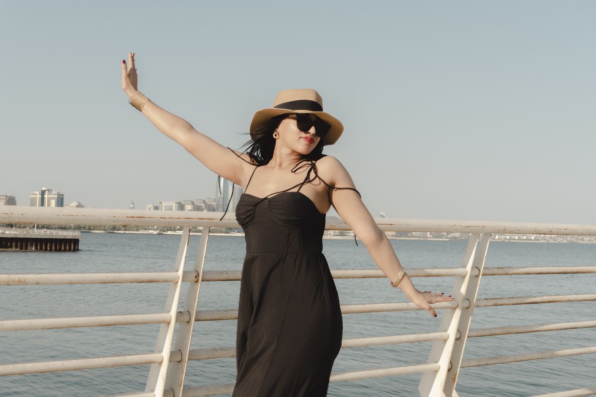 Woman in a summer dress and hat posing on a sunny day by the sea in Baku, Azerbaijan.