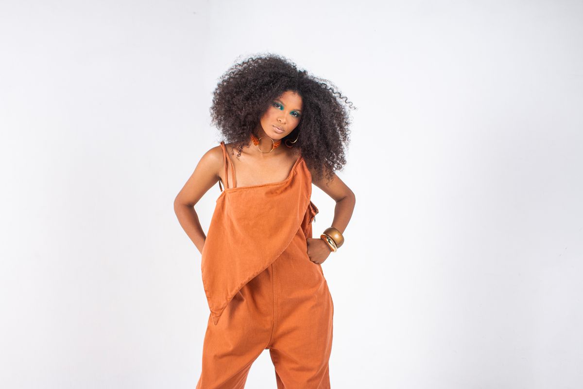 Stylish woman posing in orange jumpsuit against a clean white background.