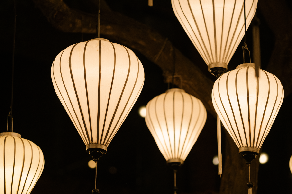 A close-up of glowing paper lanterns hanging at night, showcasing warm light and elegant design.