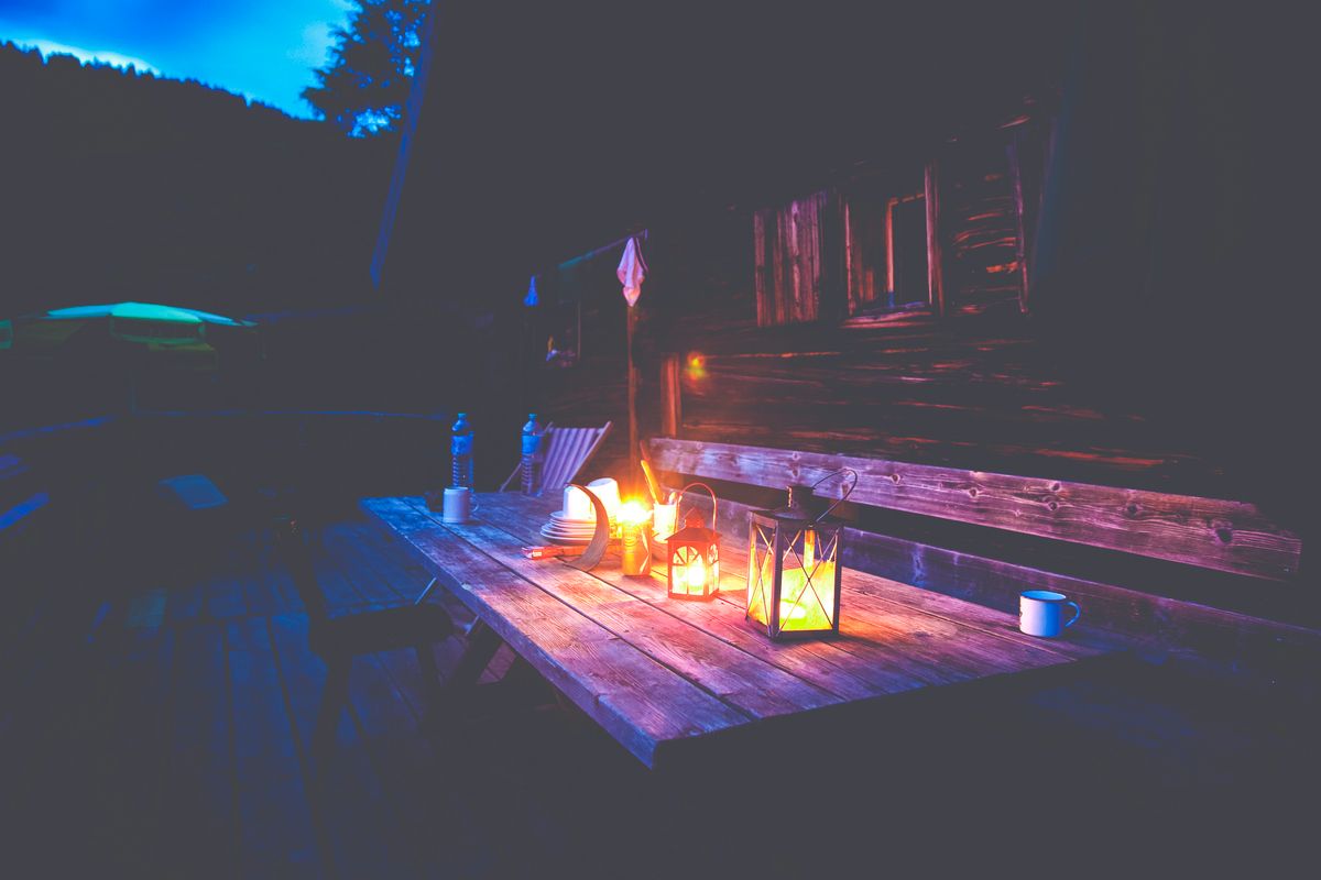 A charming outdoor scene with a candlelit table outside a rustic wooden cottage at night.