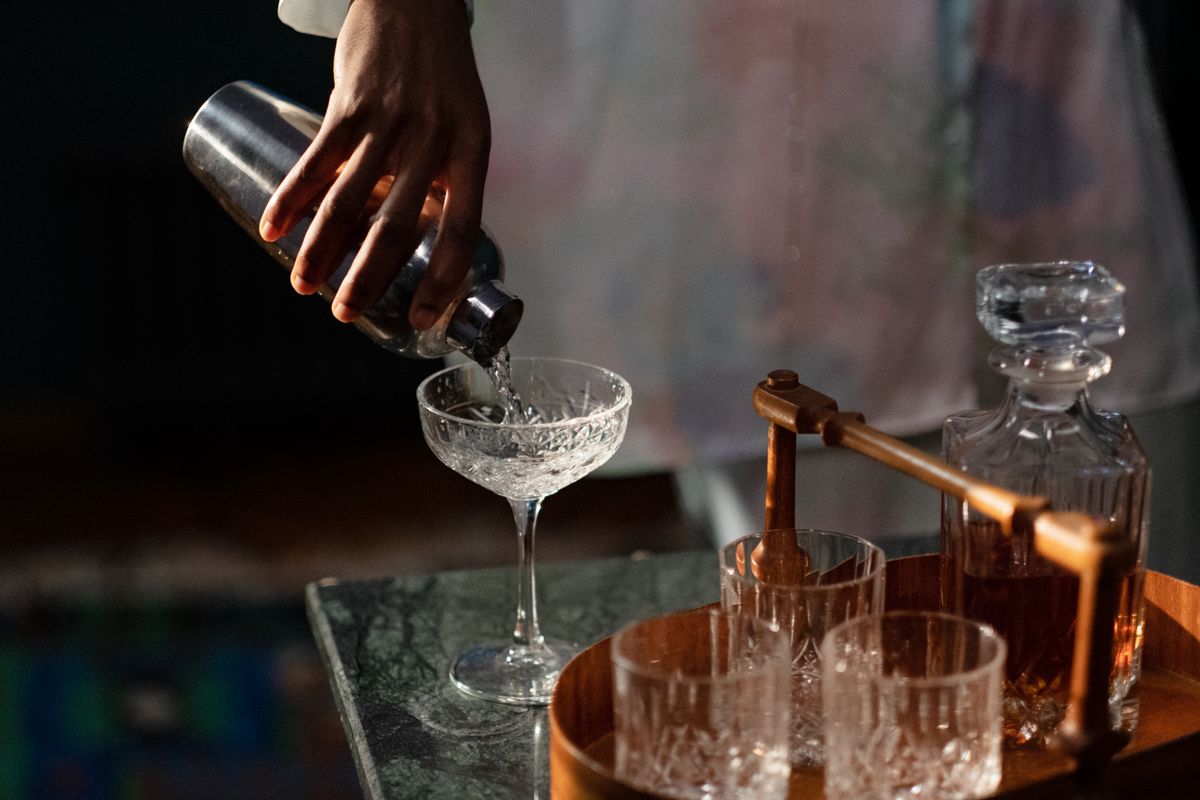 A bartender pours a cocktail into a glass from a shaker, set in a cozy home bar.
