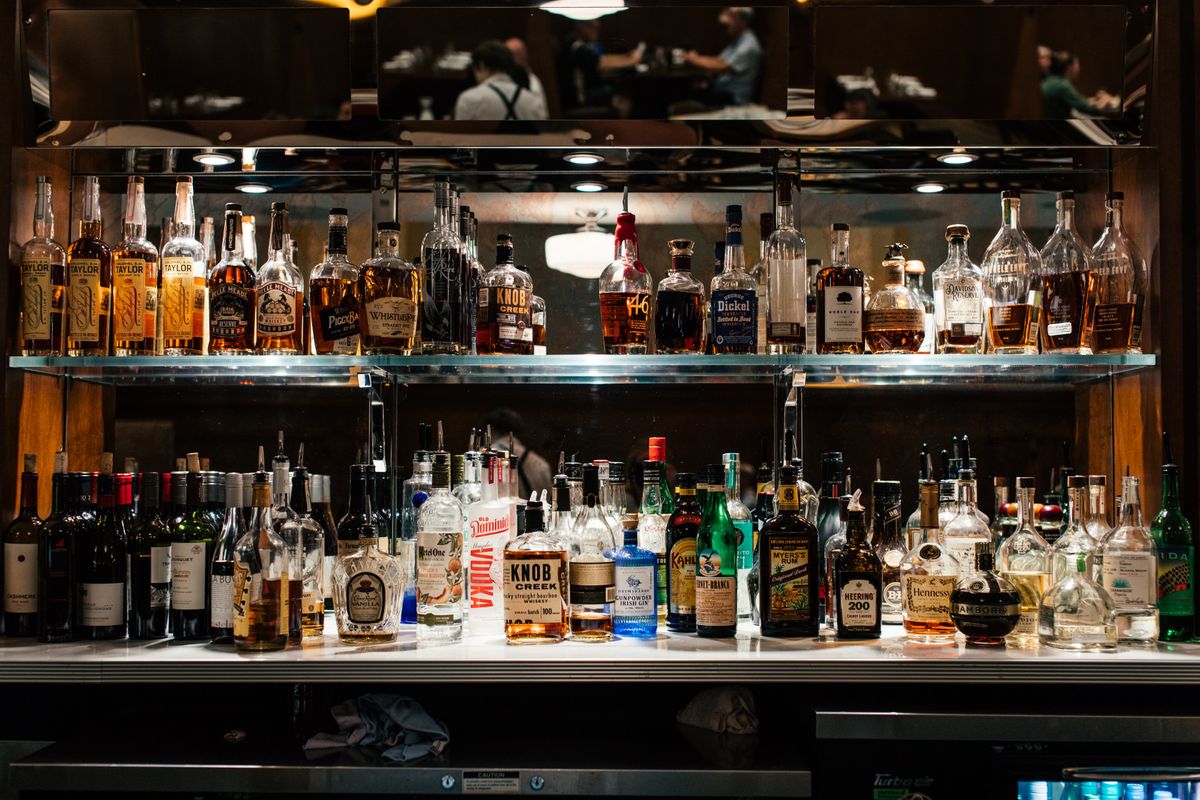 A diverse collection of liquor bottles showcased on a well-lit bar shelf.