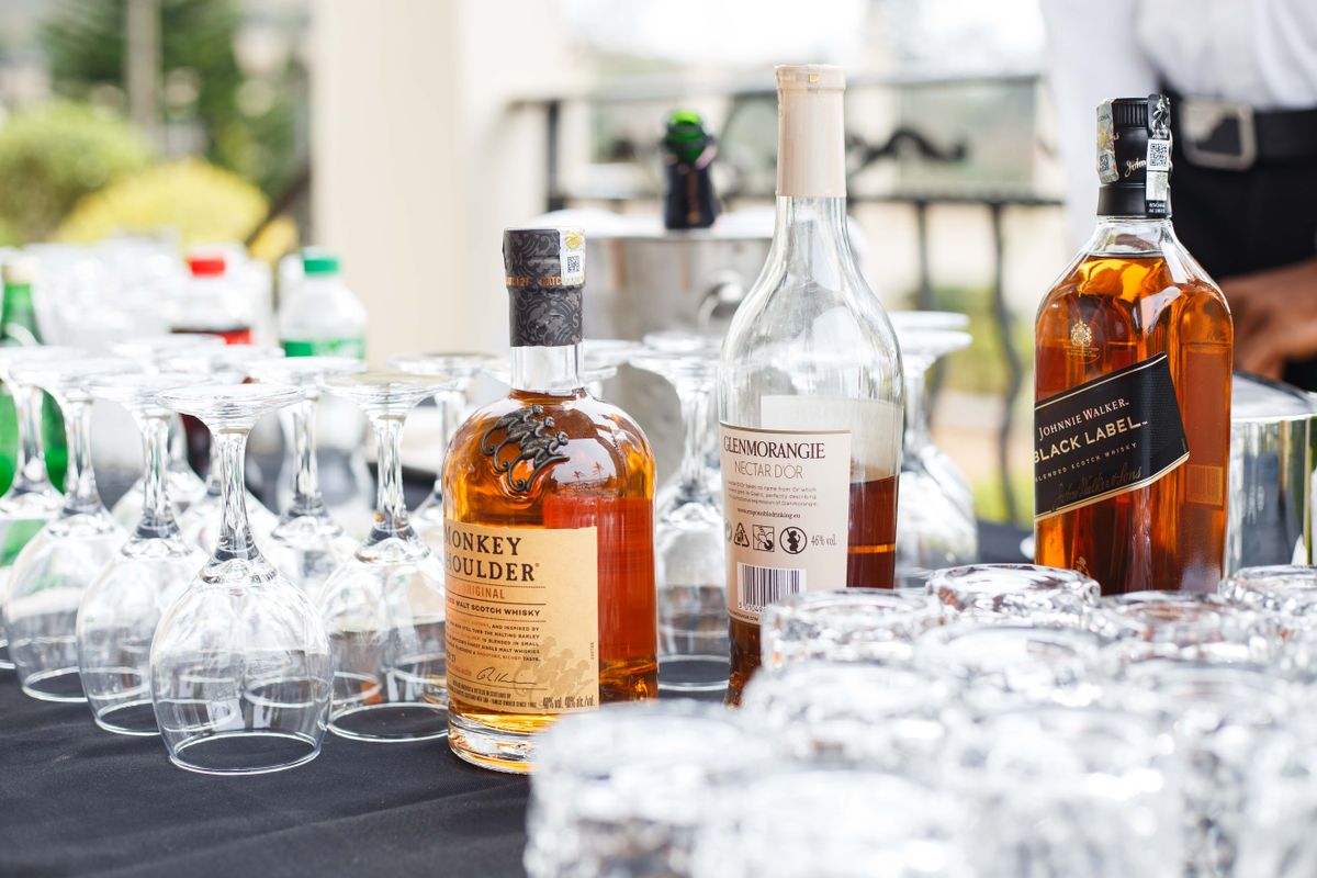 A selection of whiskey bottles arranged with empty glasses on a black tablecloth outdoors. Ideal for parties.
