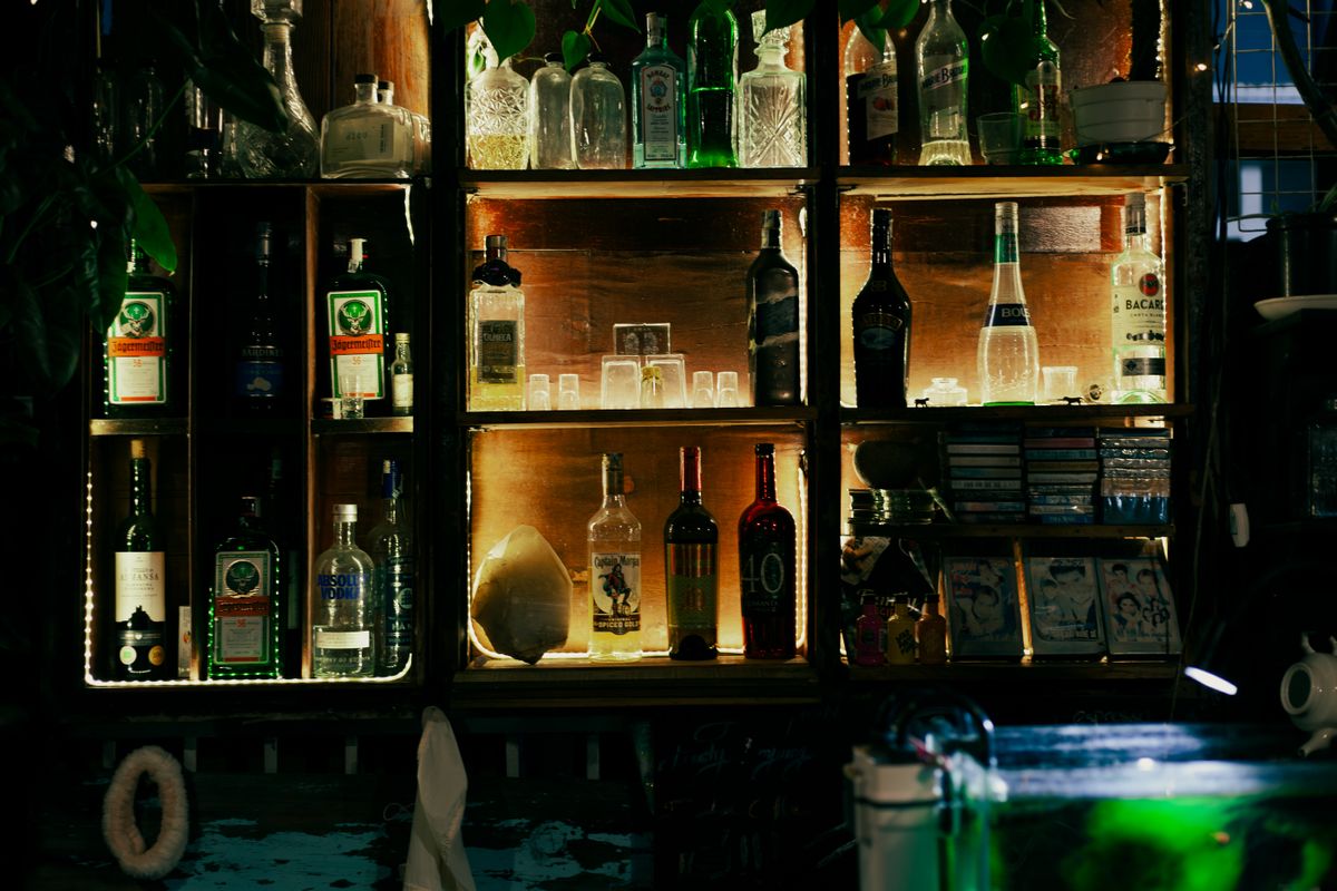 A glowing bar shelf displaying various liquor bottles and glasses in a dimly lit setting.