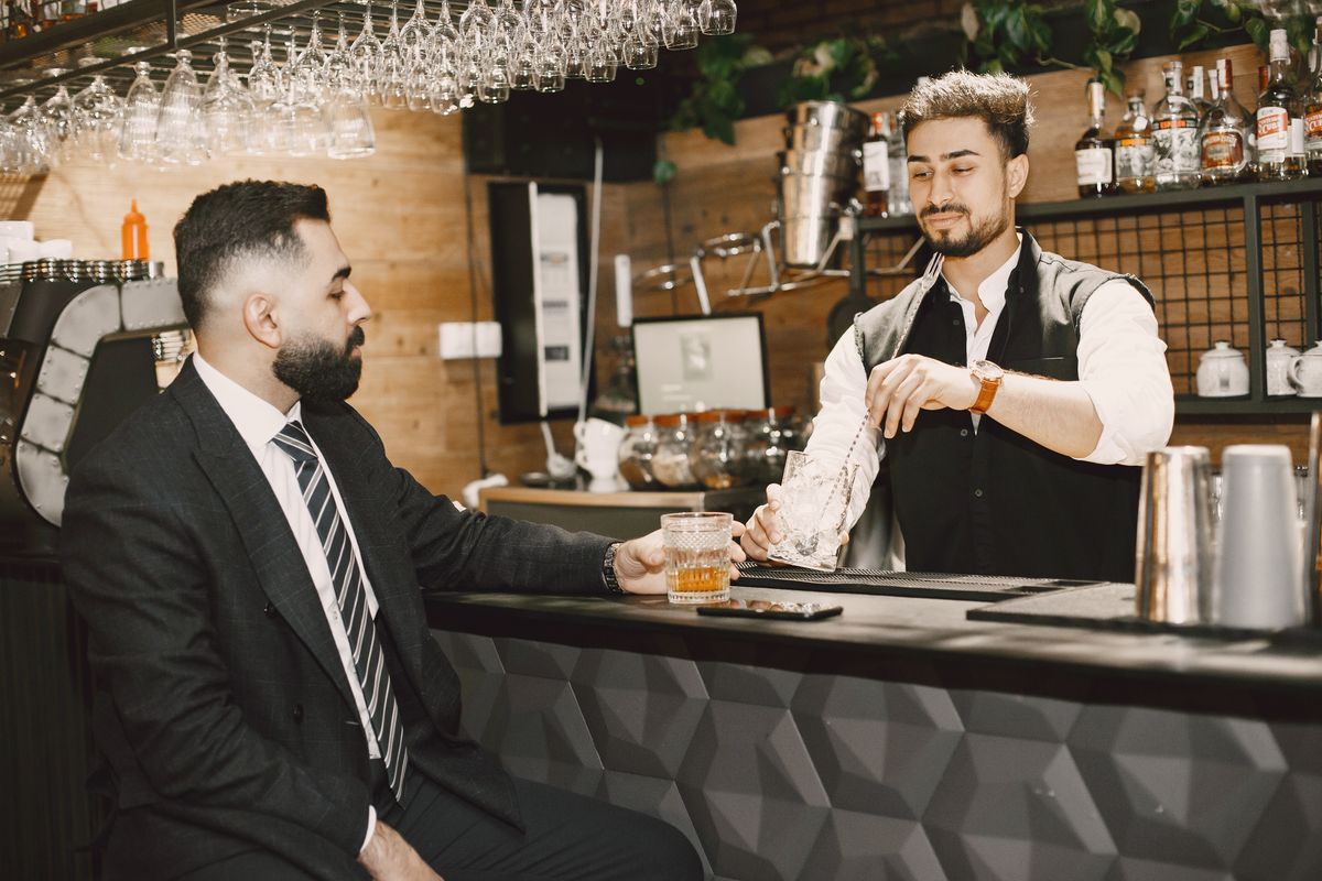 A businessman in a suit enjoying a whiskey at a modern bar with a friendly bartender.