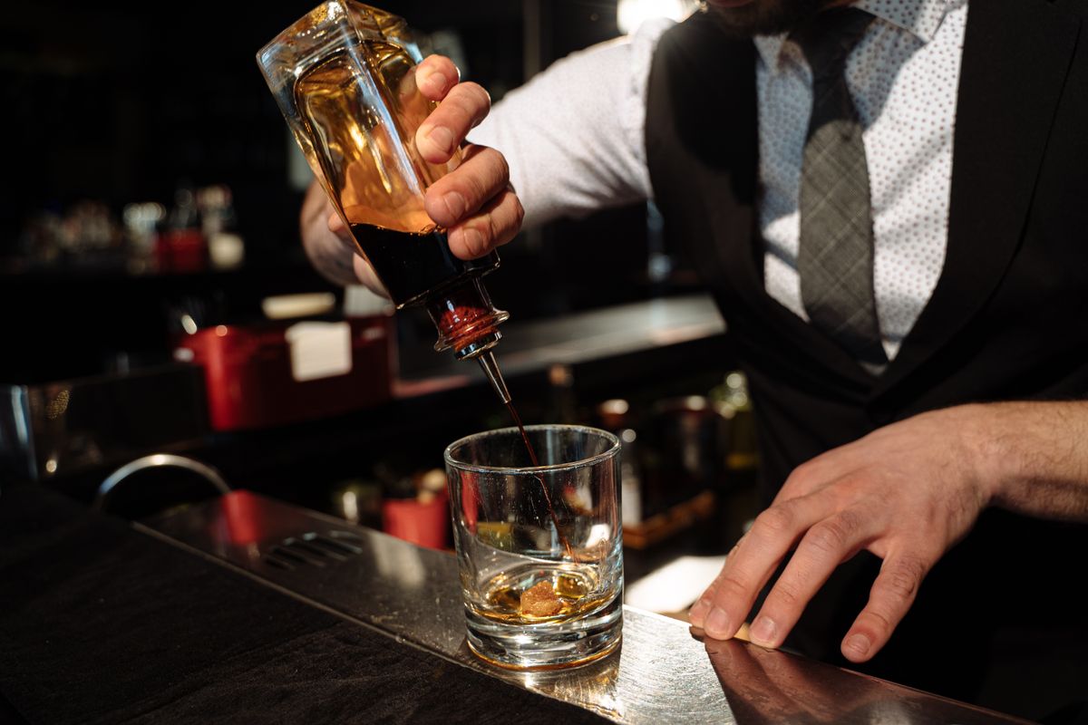 Close-up of bartender pouring whiskey into a glass at a bar counter.