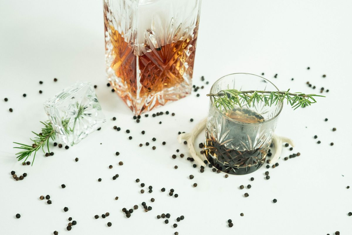 Elegant setup of whiskey glass with rosemary and pepper on white background.