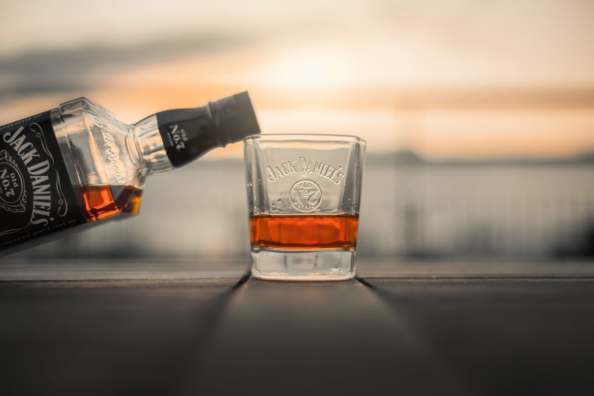 Bottle of whiskey being poured into a glass with a sunset backdrop.