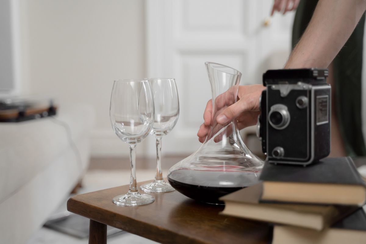 A vintage camera rests beside a decanter and glasses on a wooden table, creating an elegant scene.