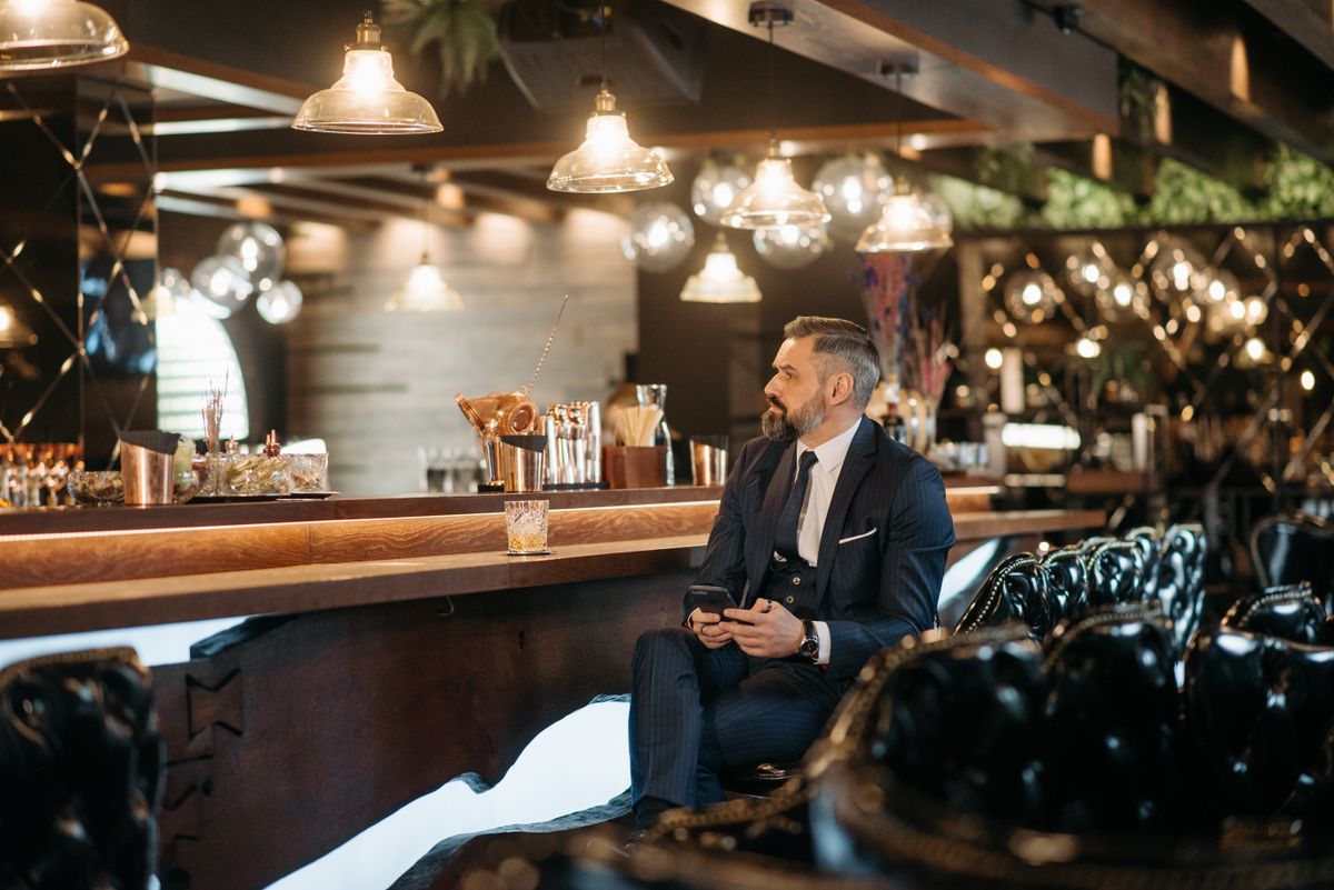 Businessman in a suit relaxes with whiskey at a trendy bar with pendant lights.