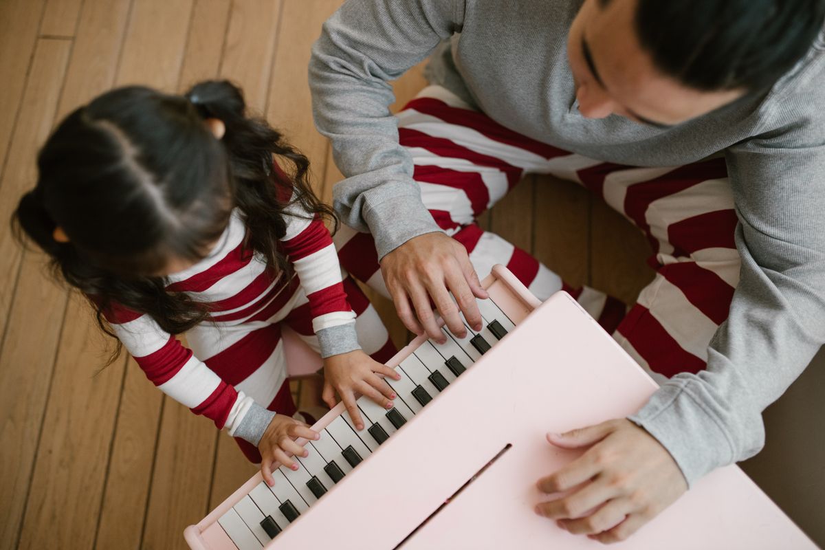 A heartwarming moment of a father and daughter bonding while playing a pink toy piano at home.