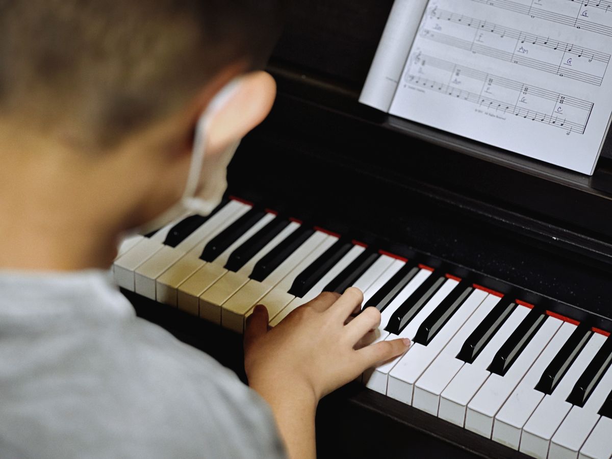 Young child learning to play piano with open sheet music, focusing on keys.