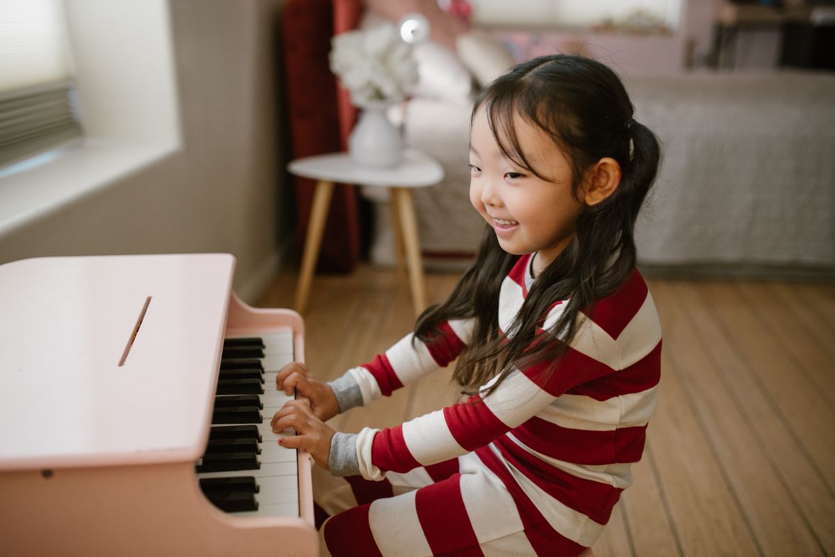 A cheerful child in striped pajamas plays a pink toy piano with enthusiasm in a cozy indoor setting.