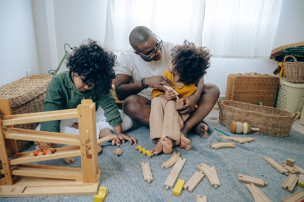 African American father in casual wear and glasses sitting on floor at home and playing with children with curly hair