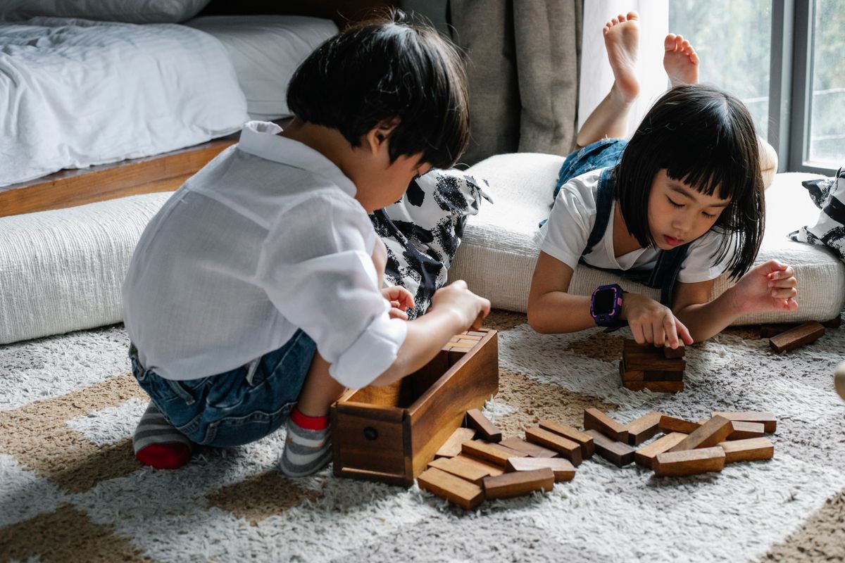 Attentive Asian boy and girl playing with tower game while sitting on floor in cozy living room in apartment