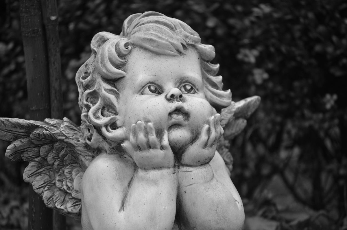 Black and white close-up of an angel statue with hands on chin, focused expression, shot in Rhede, Germany.