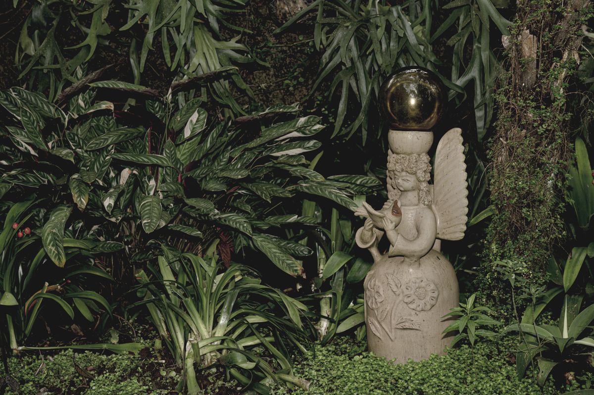 Stone angel sculpture surrounded by lush tropical foliage in a serene garden setting.