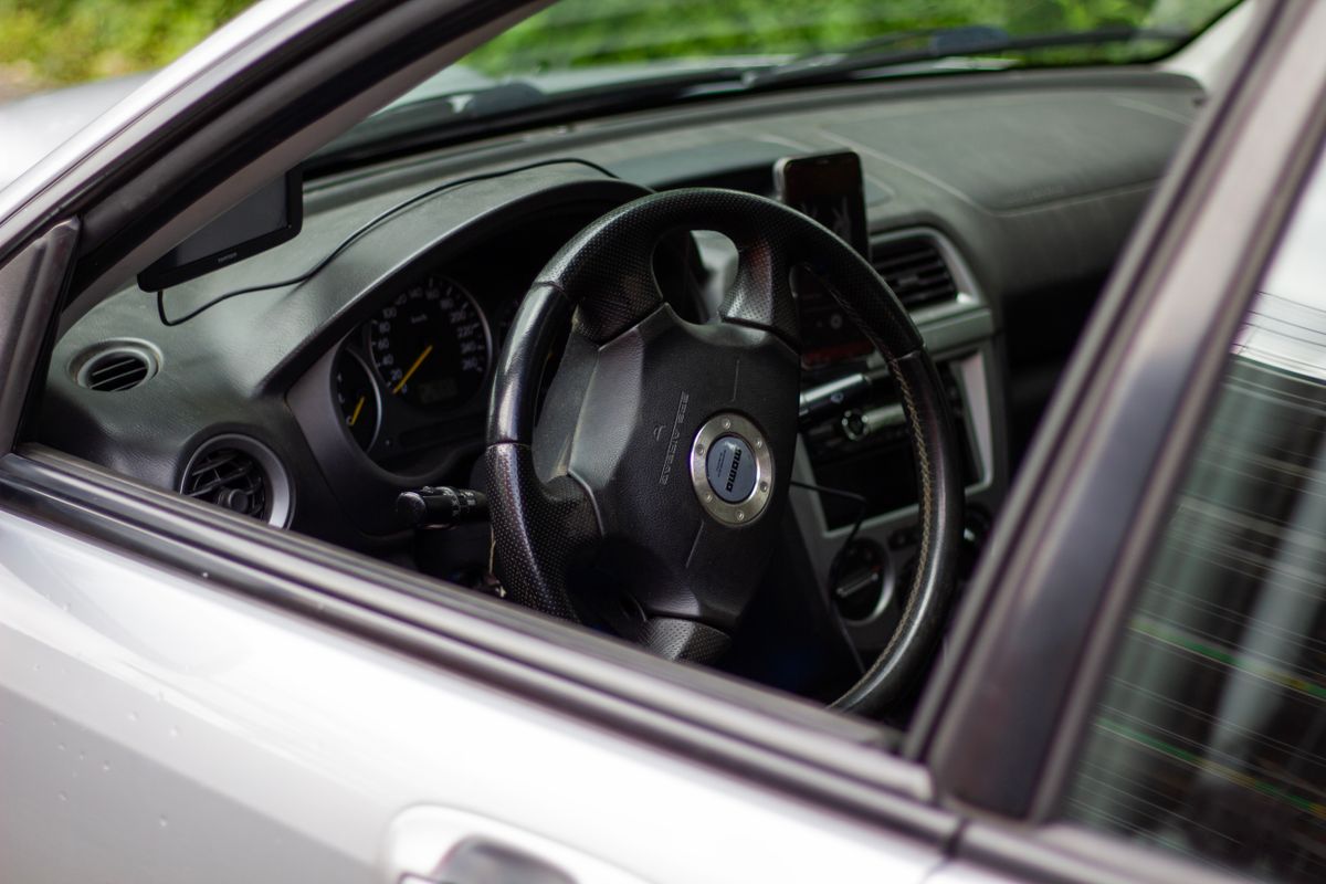 Close-up of a car's interior showing the steering wheel, dashboard, and open window.
