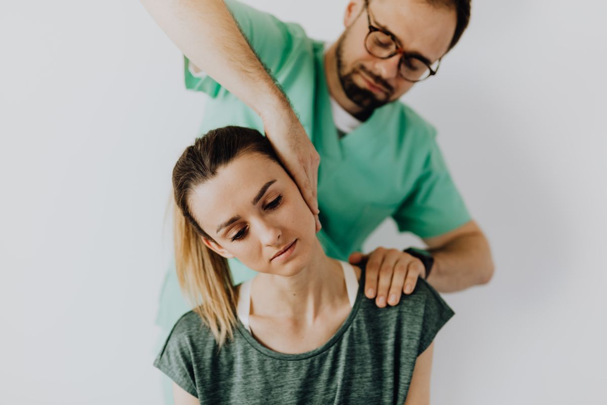 Concentrated doctor massage therapist in medical uniform doing therapeutic neck massage for calm young female patient in casual wear