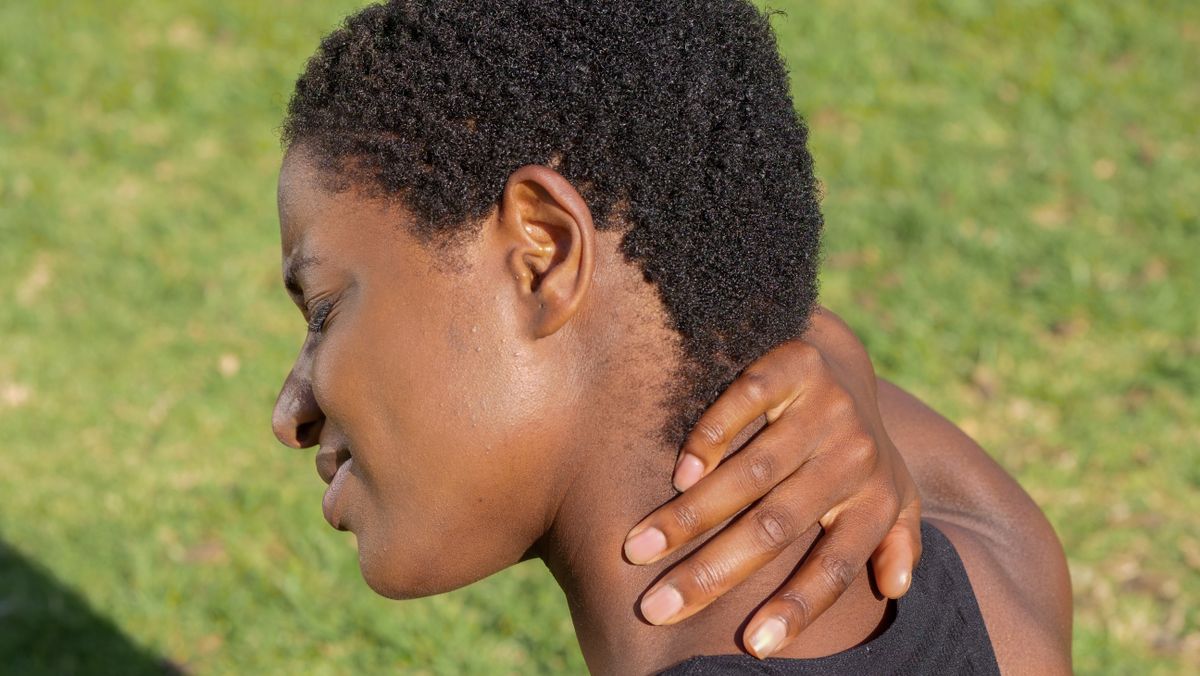 African American woman touching neck outdoors, experiencing discomfort.