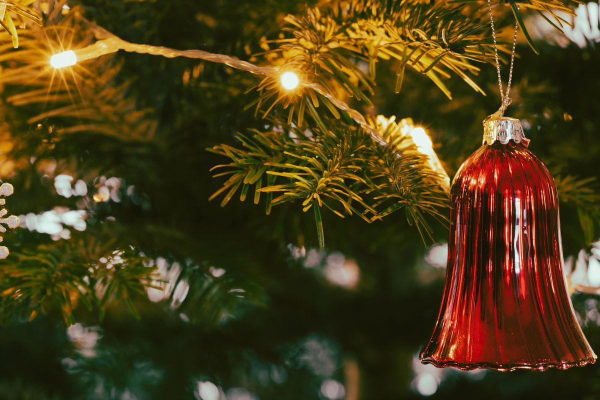 Close-up of a red glass bell ornament on a Christmas tree, illuminated by warm lights.