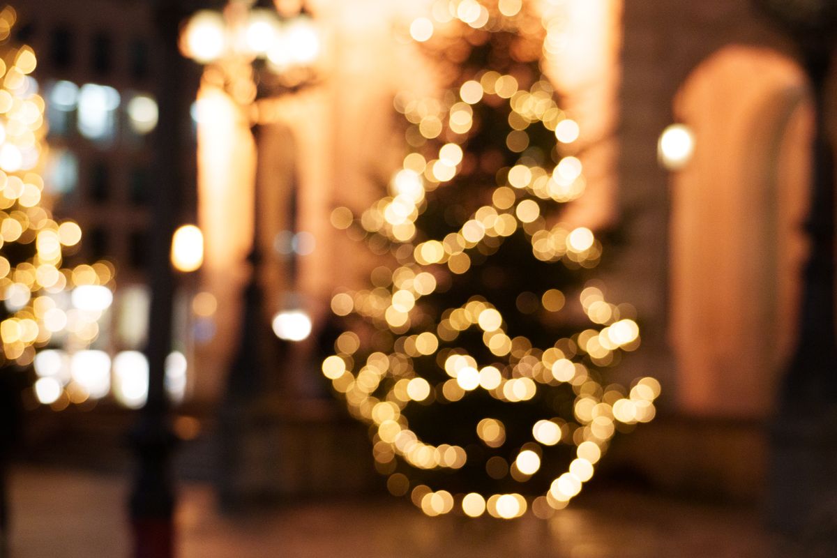 Blurred view of a Christmas tree with twinkling lights in an urban, festive atmosphere.