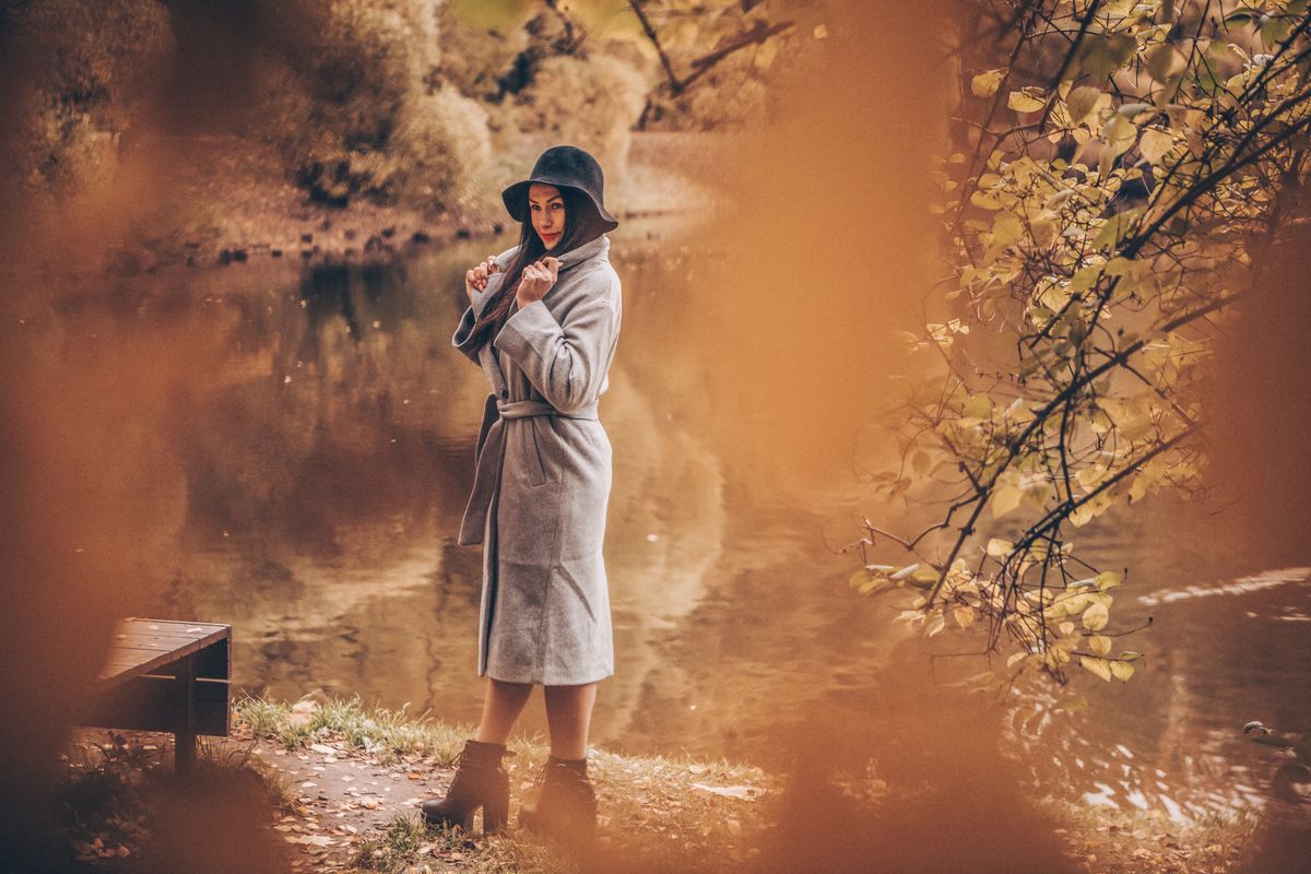 Woman in a coat by a serene lake during autumn, showcasing seasonal fashion.
